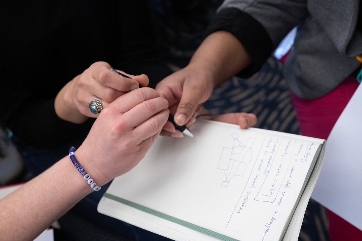 Three individuals writing in a notebook, highlighting a shared effort in documenting thoughts or ideas.
