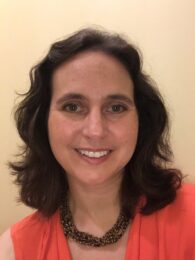 smiling woman in red blazer in front of beige wall