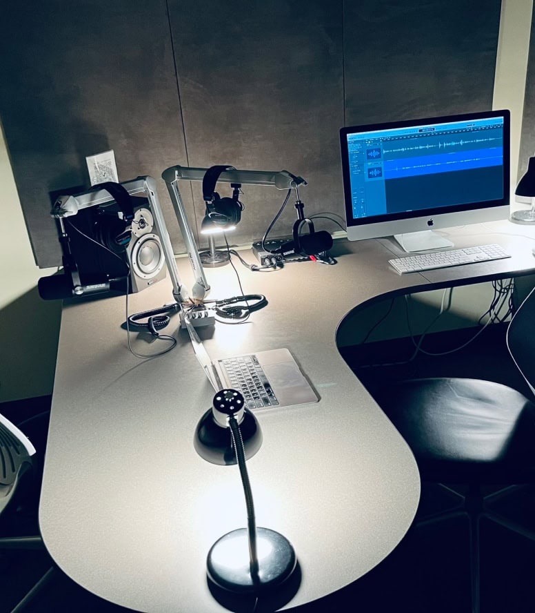Podcast studio desk with computer and microphone.