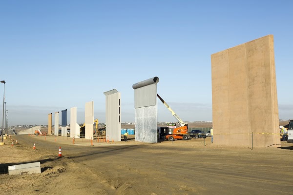 Border wall prototypes spaced apart with a blue sky in the background. The walls are light brown, gray and cream.