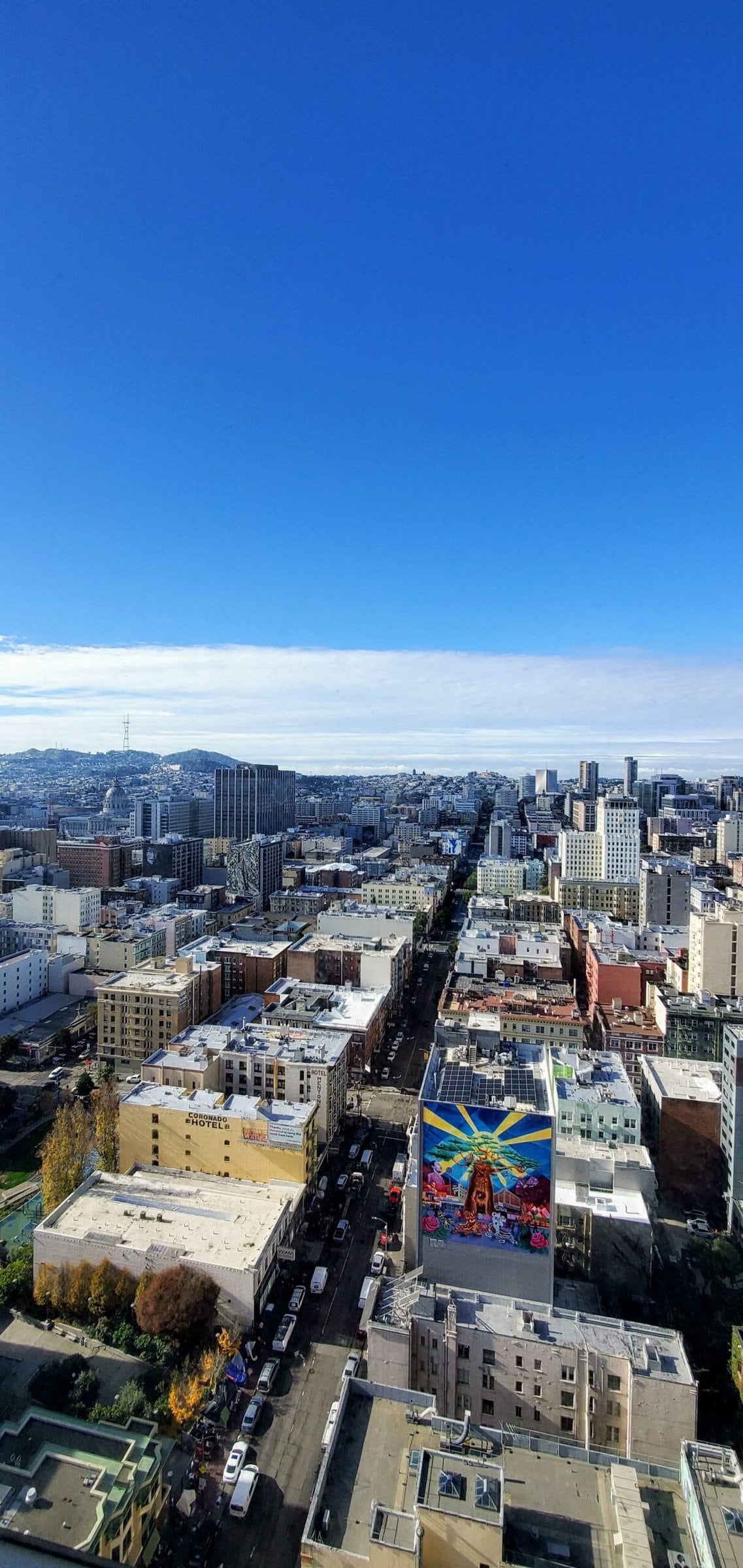 A high up view of a city street. The sky is blue and there are many buildings.