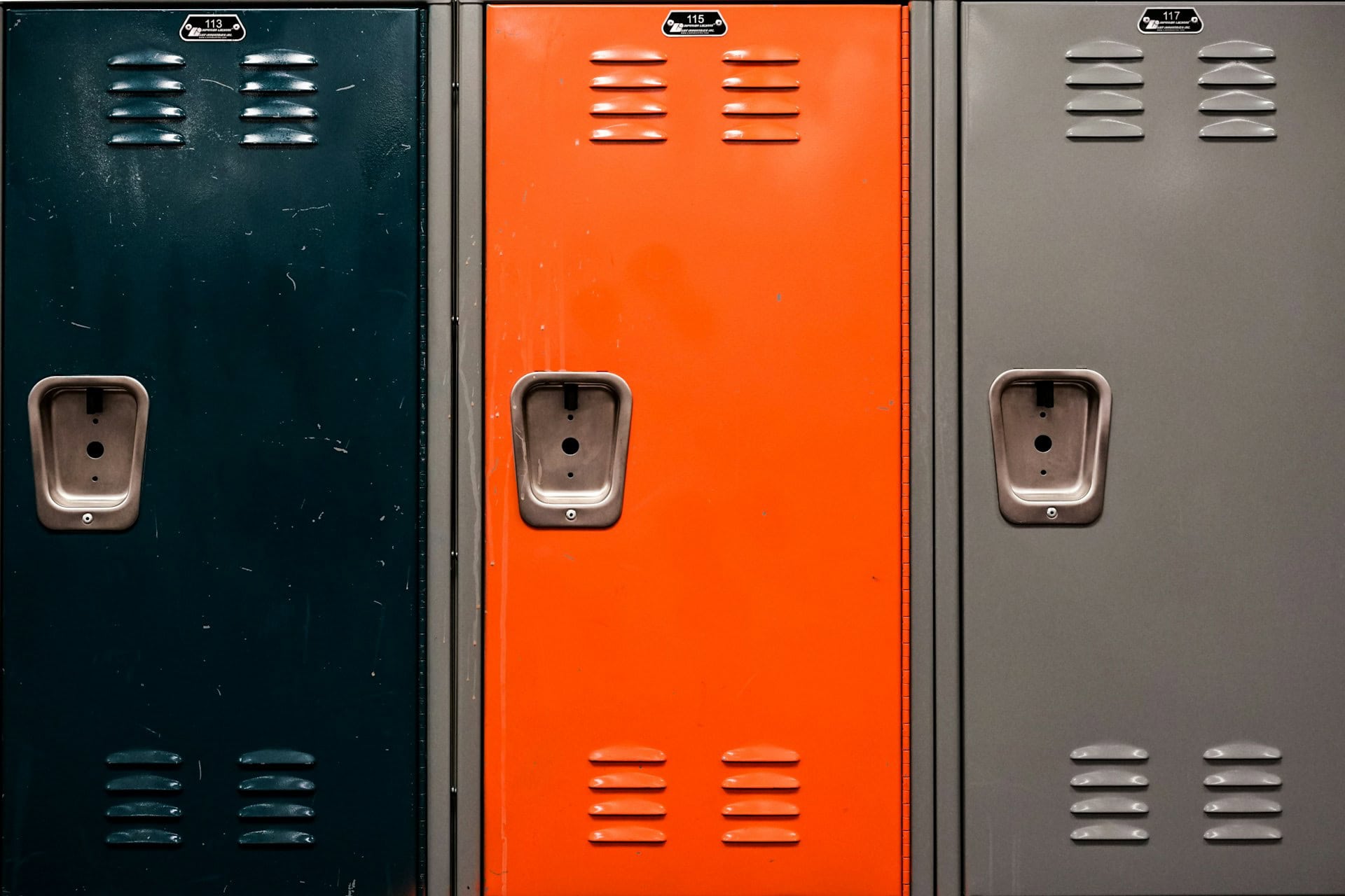 Three metal school lockers in a row, one dark blue, one orange, one gray.