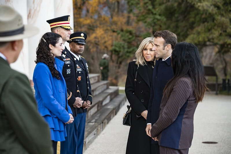 Two rows of six people stand facing each other in front of marble columns. In the foreground on the left is a white woman in a bright blue coat. Behind her are two men in military uniform. They face on the right side a blond woman, a man, and brunette woman. Close to the camera on the left side is a person in a National Parks Service uniform.