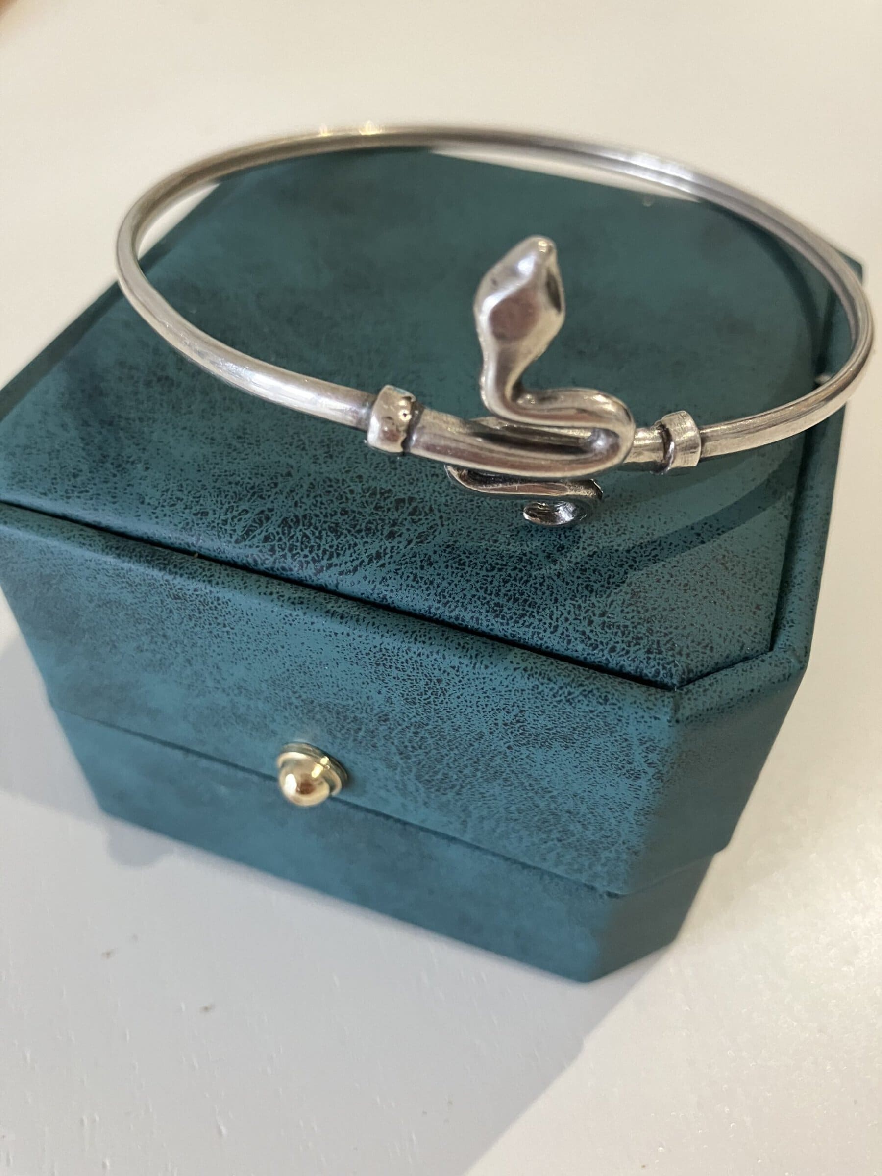 A silver bracelet decorated with a snake sits atop of a small green jewelry box.