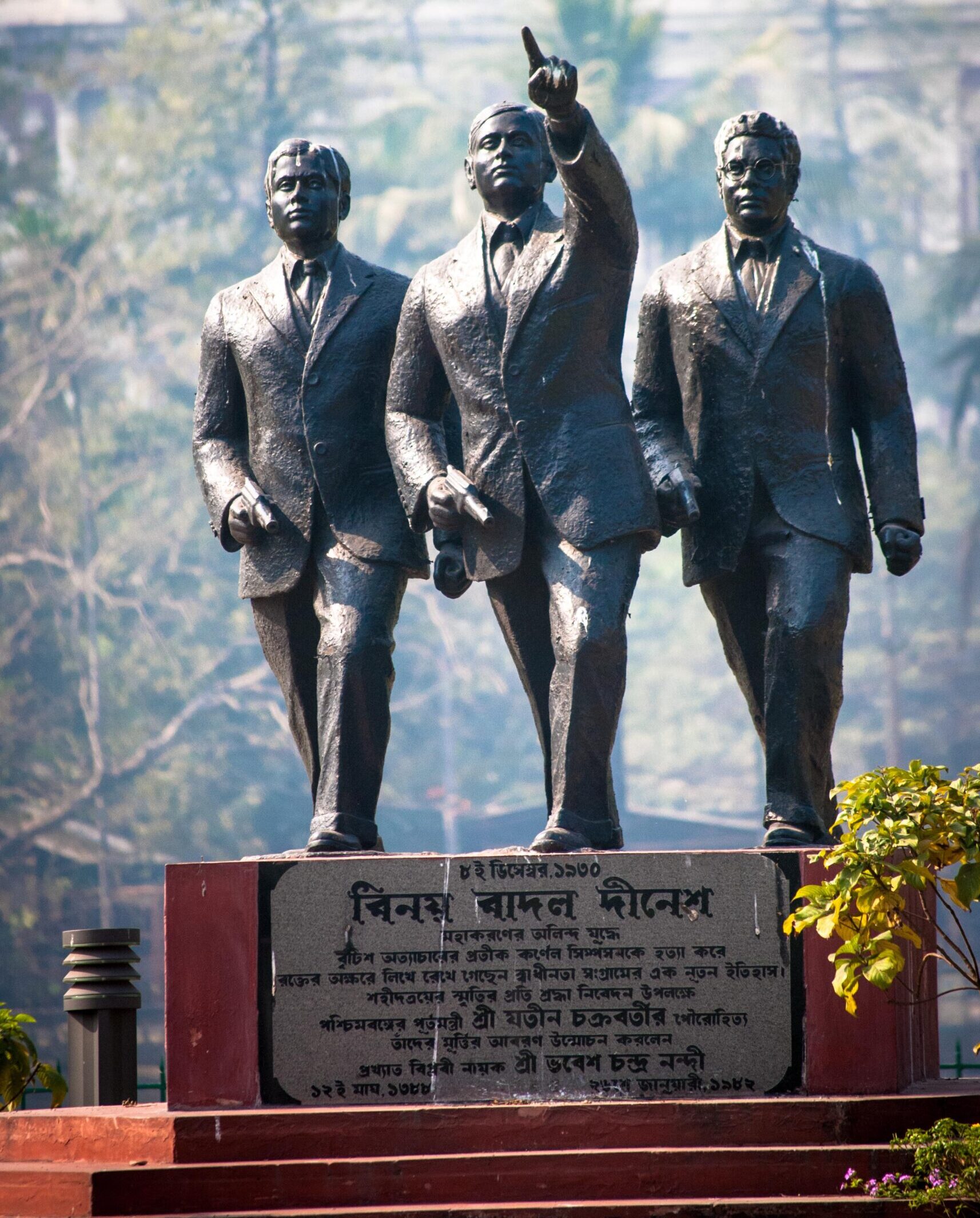 A statue of three young men on a plinth. All three are wearing suits and holding pistols. The man at the center points ahead with his left hand.